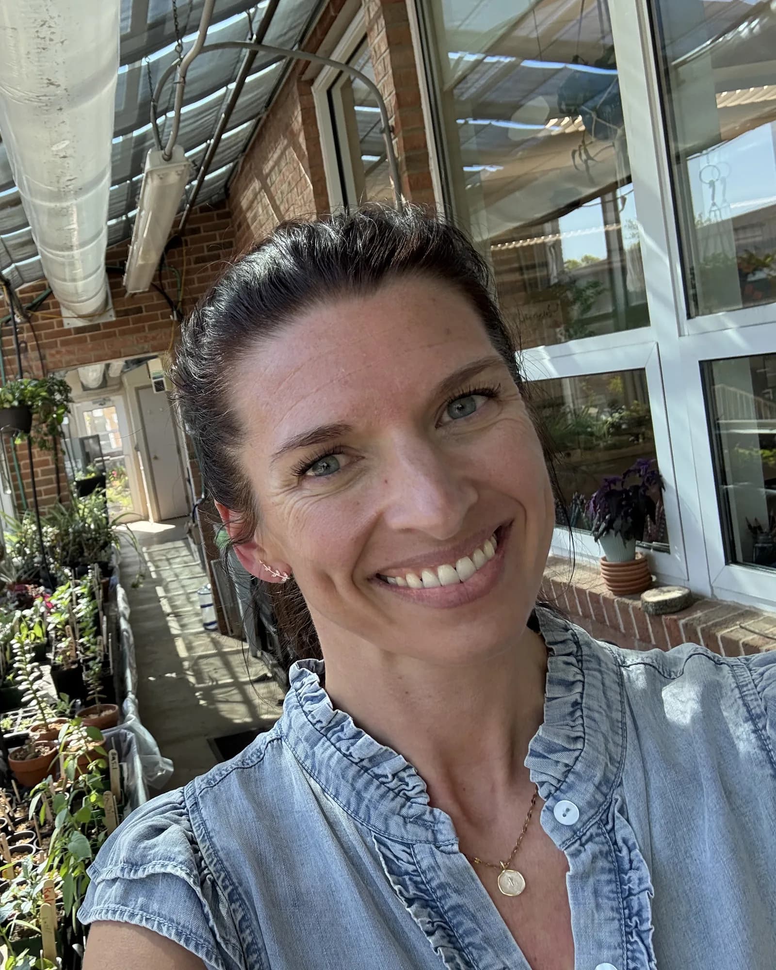 Mrs. Denise smiling in her classroom greenhouse full of seedlings.